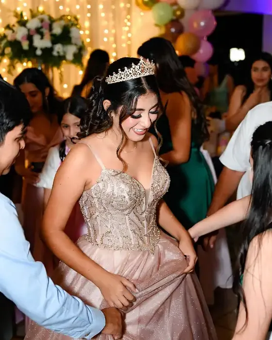 Quinceañera con vestido rosa baila entre los invitados en un salón decorado con globos.