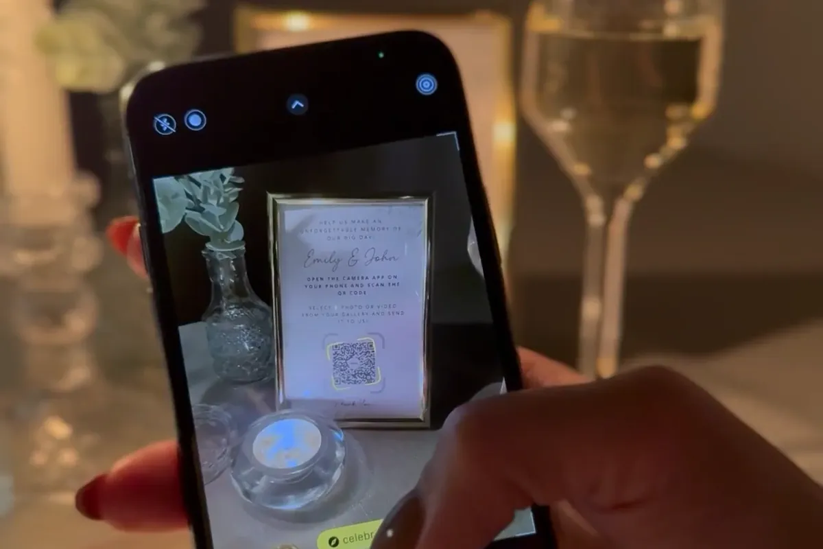 Telefon skanuje kod QR z kartki w ramce na weselnym stole przy świecach.
